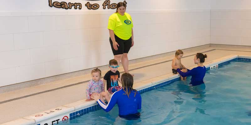 A poolside deck supervisor overseeing two swim teachers and three young children in the pool at Njswim school