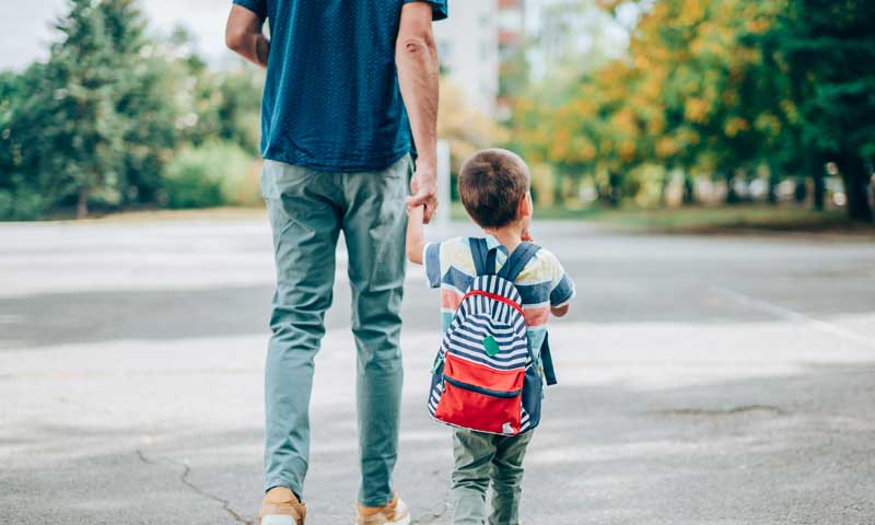 A young boy walking home from school with parent