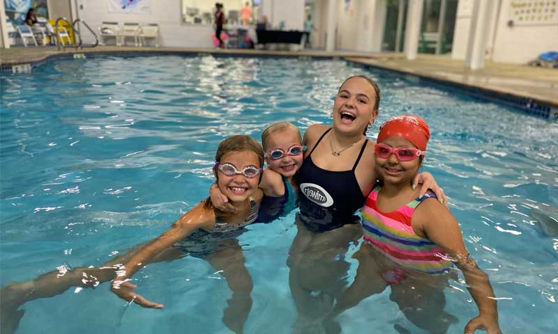 An Njswim teacher with three smiling swim students in the pool