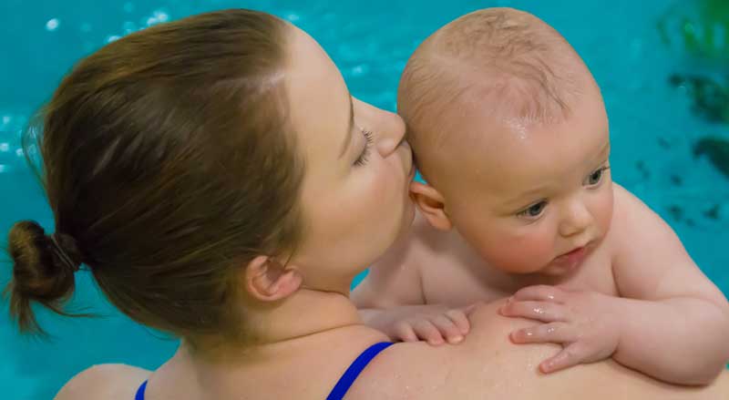 A woman holding and kissing her baby during an infant swim class