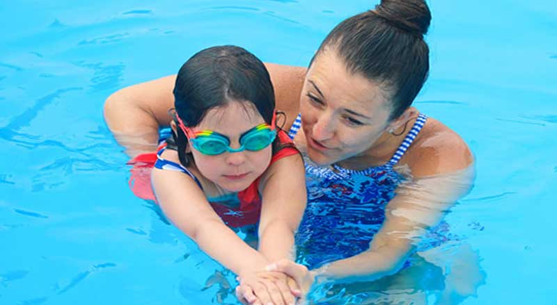 A young girl in a swimming pool with her swim teacher
