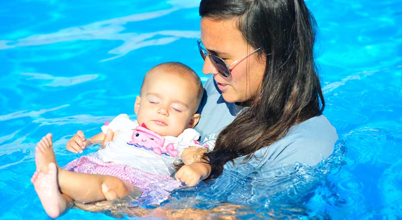 A young baby girl is supported by woman in pool