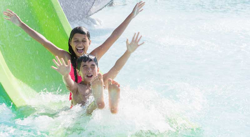Two kids going down a slide together in a water park