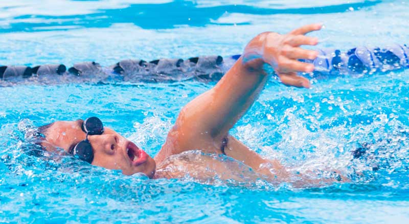 Older boy wearing swim goggles while practicing the front crawl in a pool