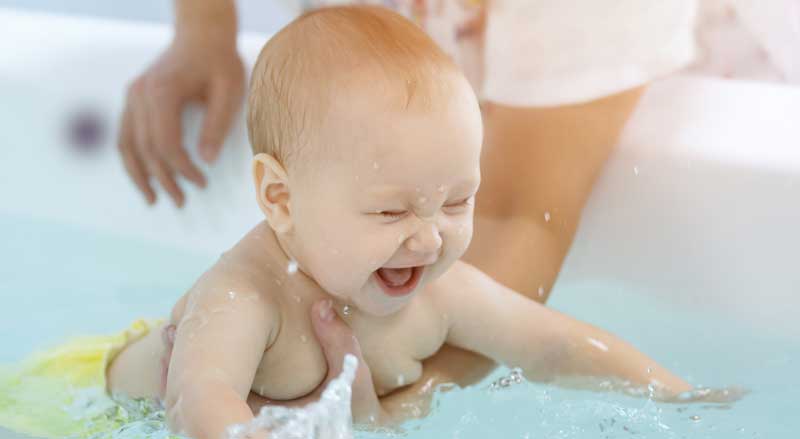 A baby girl is smiling and laughing while she splashes in the water.