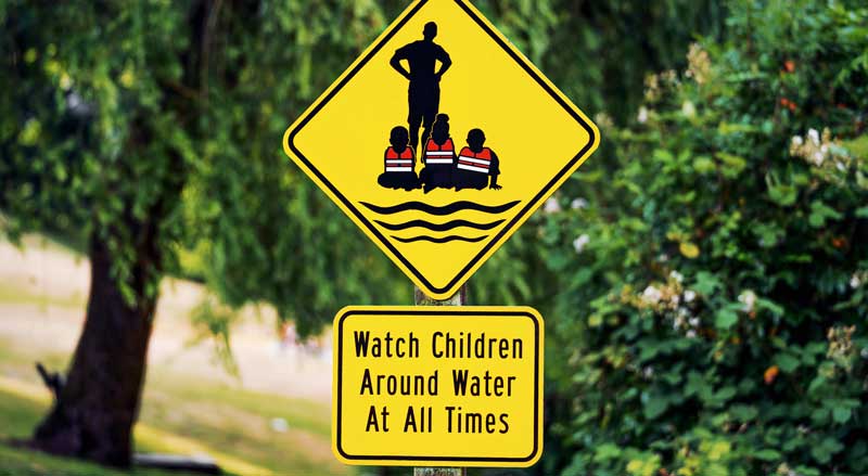 A sign at the lake's swimming area reminds adults to supervise children, reading "Watch Children Around Water At All Times."